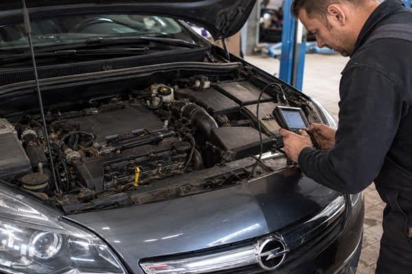Opel Astra garée dans un atelier, capot ouvert, moteur visible, et un mécanicien en train de réaliser un diagnostic avec une valise OBD