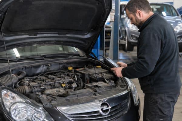 Opel Corsa d’occasion dans un atelier ou un garage, capot ouvert, avec un mécanicien en train de contrôler le moteur